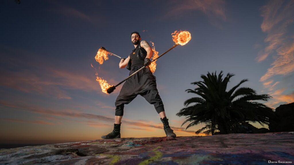 fire performer holding two fire staffs