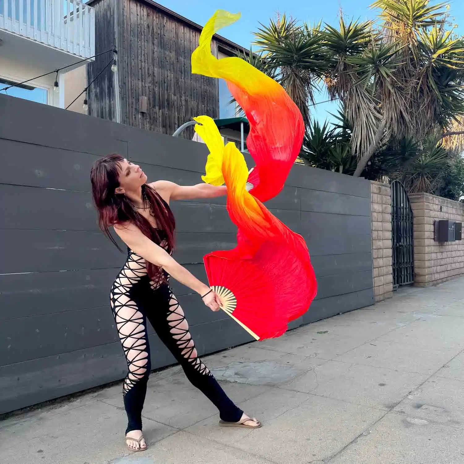 action shot of a performer using silk fans that are orange red and yellow
